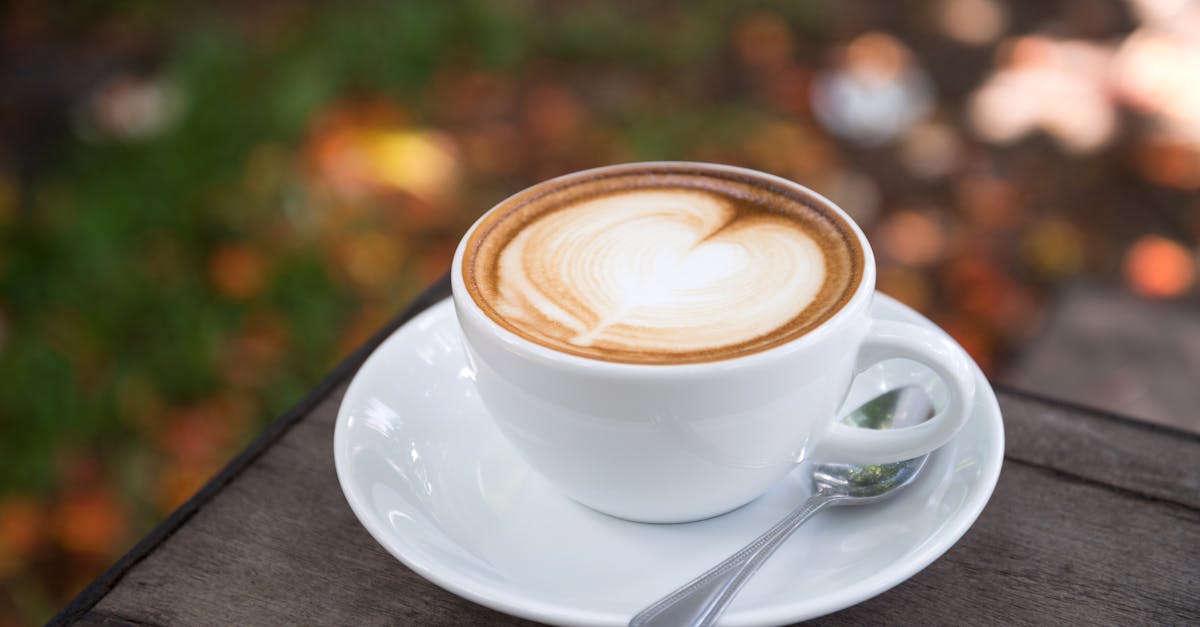 A beautifully crafted latte with heart art sits on a wooden table outdoors.