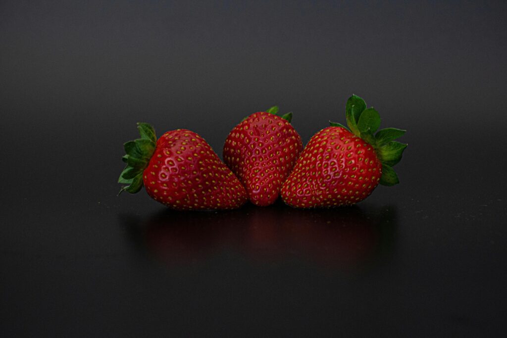 Close-up of three fresh strawberries on a dark surface, perfect for healthy and organic food concepts.