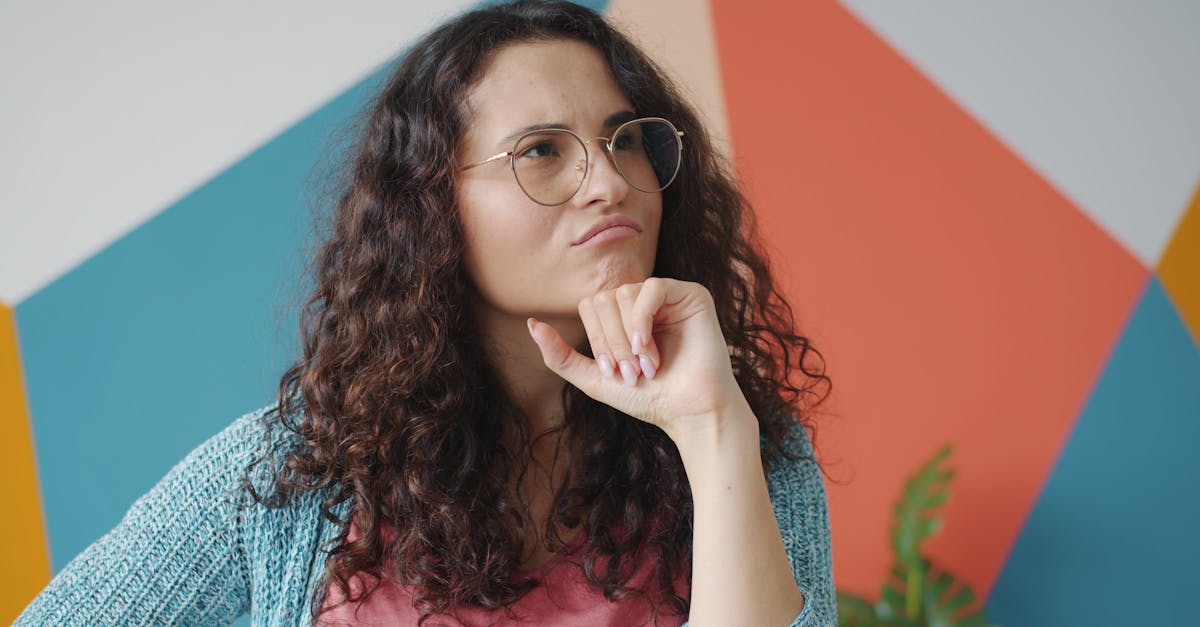 Curly-haired woman in glasses thinking against a colorful geometric backdrop.