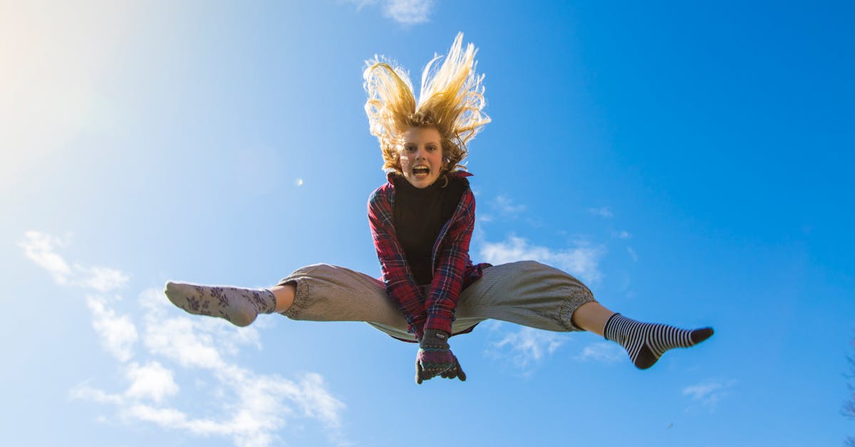 A girl energetically jumping under a clear blue sky, expressing freedom and joy.