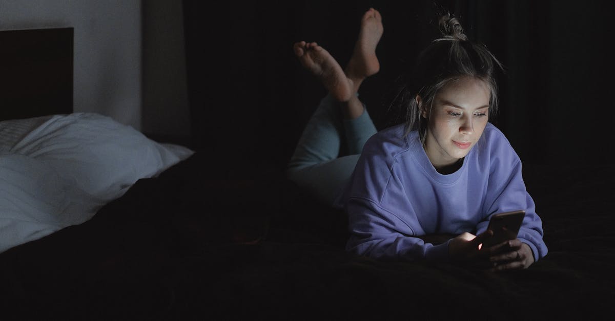 A woman lies in bed at night, using her smartphone with a relaxed expression.